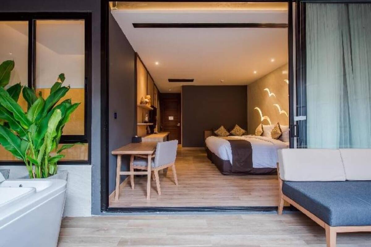 Ein modernes Hotelzimmer mit Bett, Sofa, Esstisch und einer großen Pflanze.