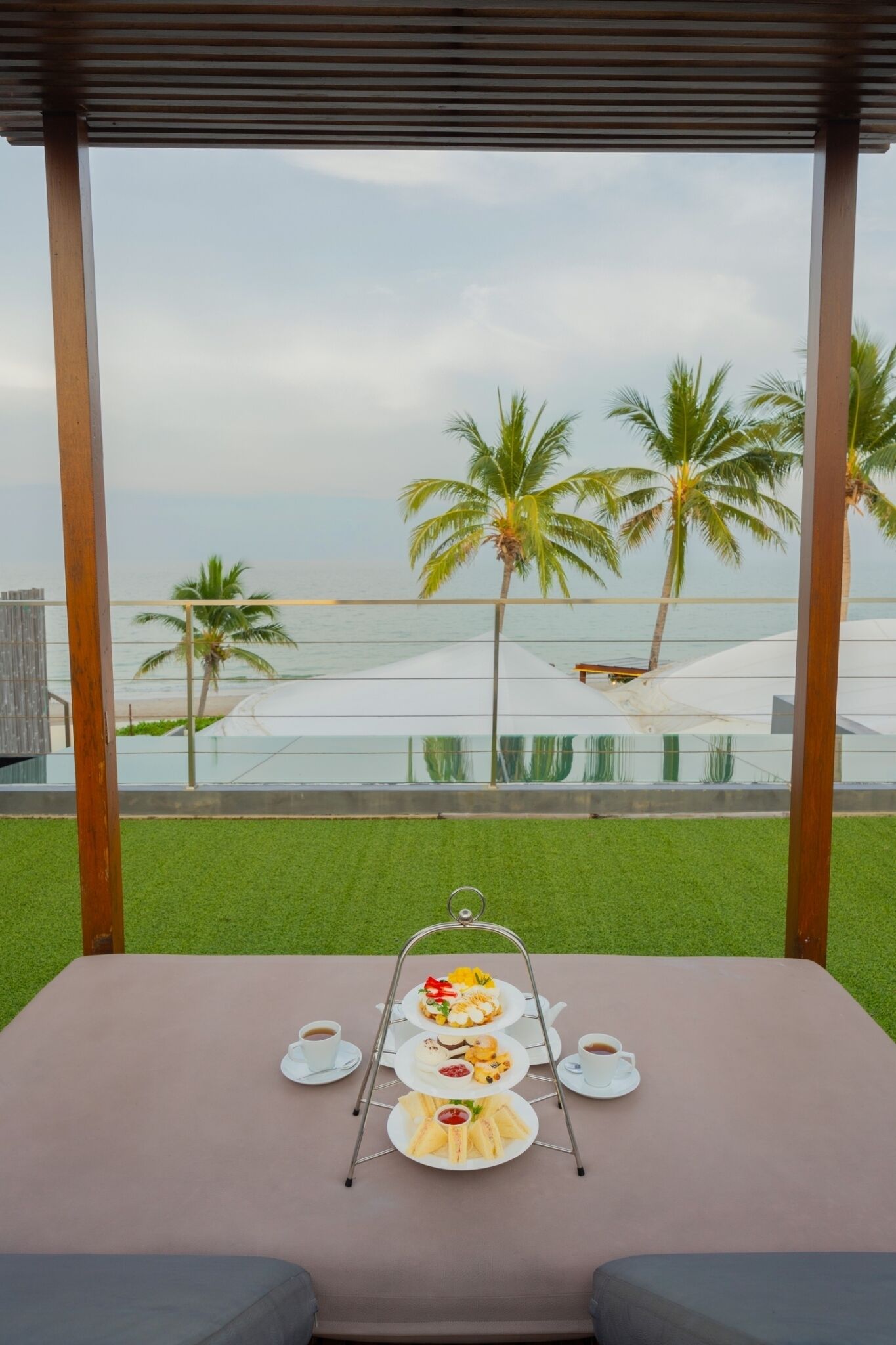 Een tafel met een drijvende etage vol eten en drinken, met uitzicht op een strand met palmbomen en een zwembad.
