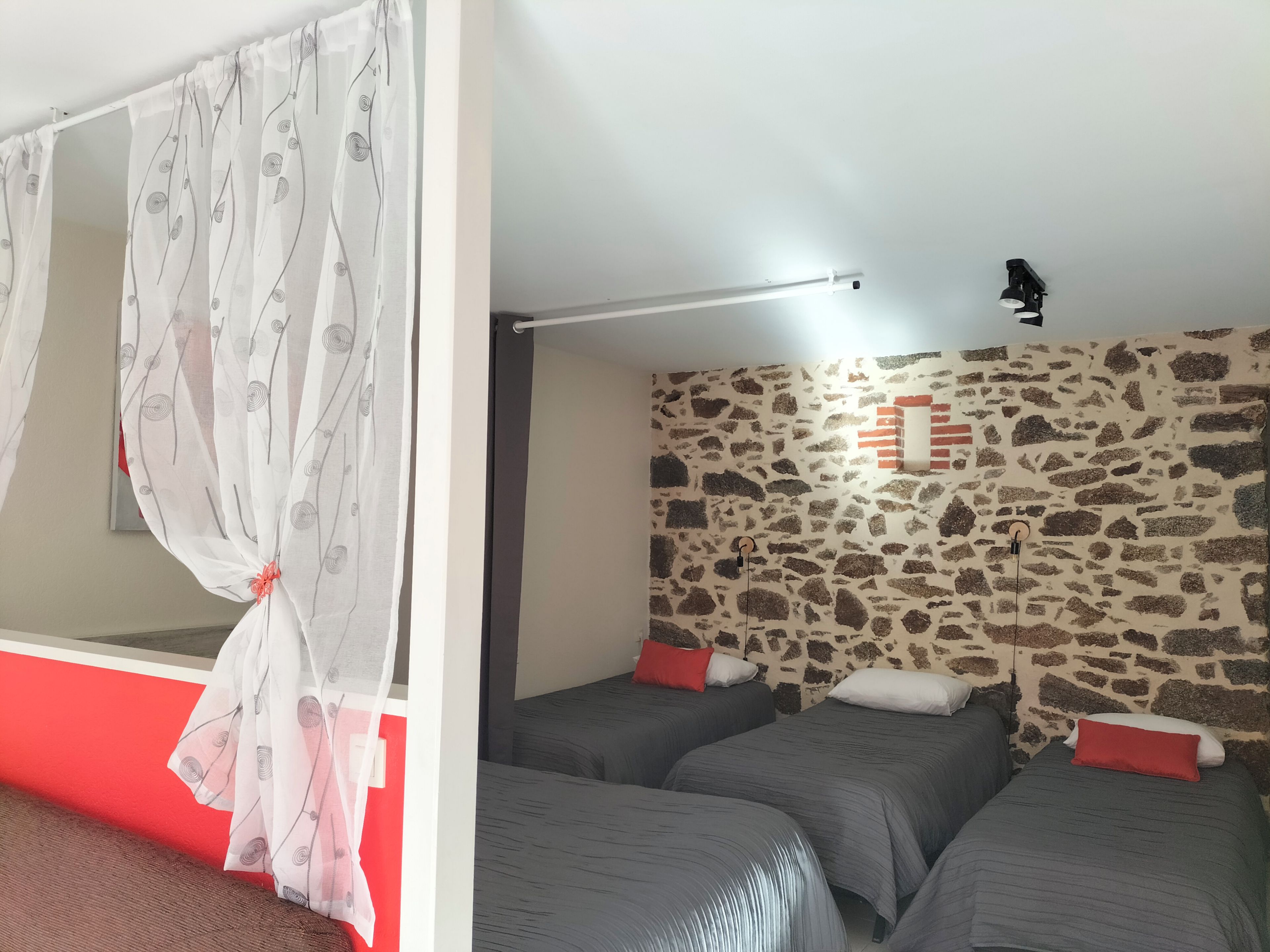 Una habitación con una cama, mosquitera, pared de piedra y una lámpara en el techo.