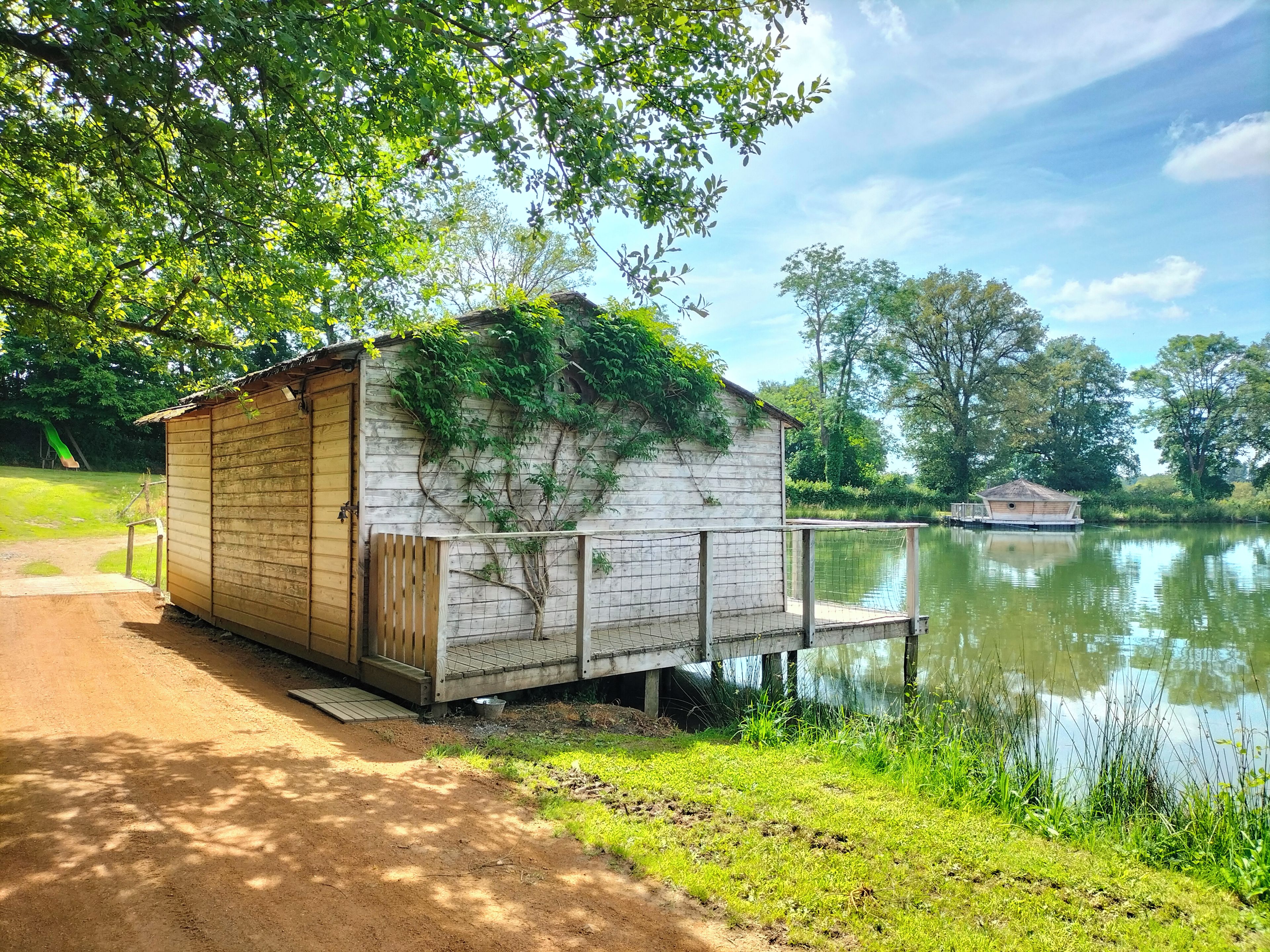 Un abri en bois avec une porte, un petit porche et une rambarde en treillis, situé au bord d’un lac paisible.