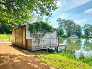 Eine Holzhütte mit Tür, einer kleinen Veranda und einem Geländer aus Netzgewebe an einem ruhigen See.