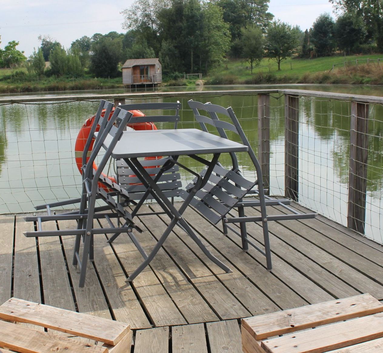 A wooden deck with a metal table and chairs, a lifebuoy, and a small shed in the background.