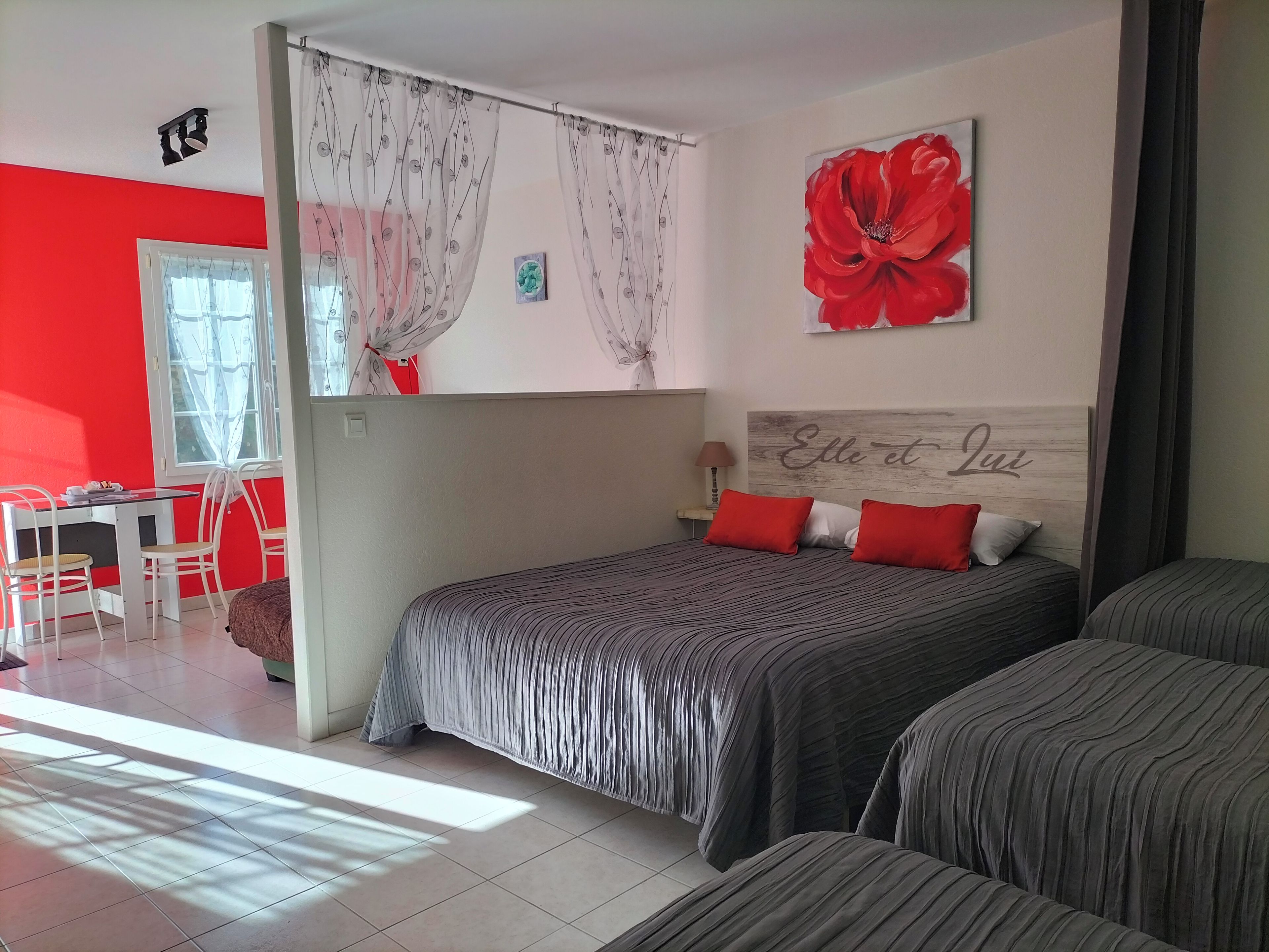 A bedroom with a bed, two bedside tables, a window with curtains, a red flower painting, and a headboard with a name.