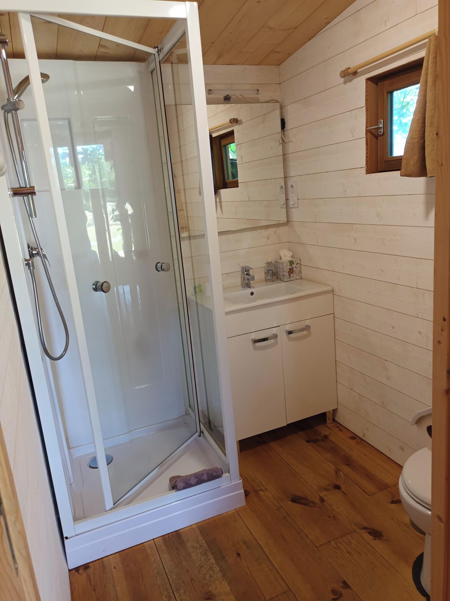 Een badkamer met een douchecabine van glas, een wastafel met spiegel en houten vloeren.