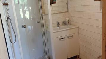 Een badkamer met een douchecabine van glas, een wastafel met spiegel en houten vloeren.