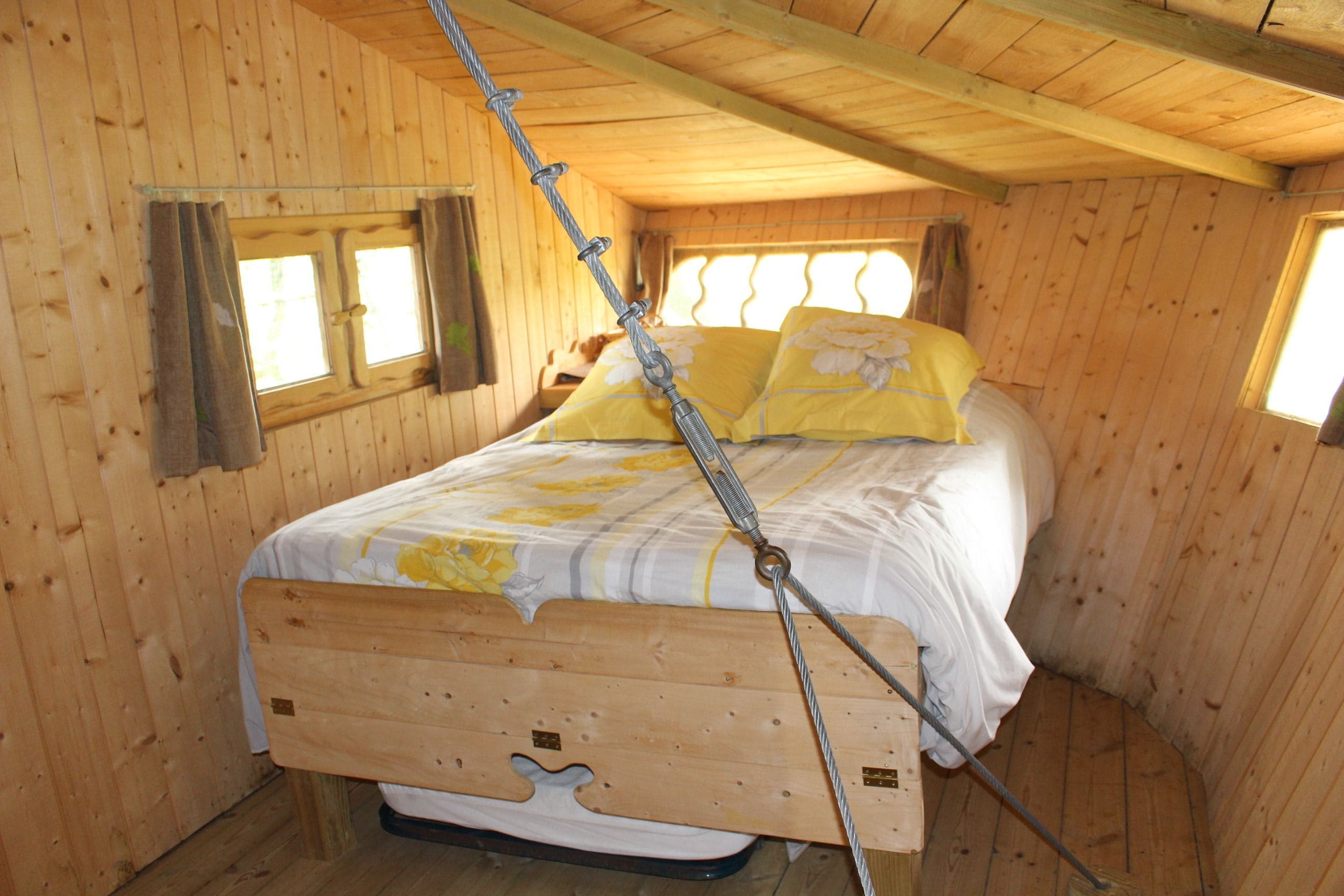 A wooden cabin bedroom with a bed, a window, and a wooden ceiling.