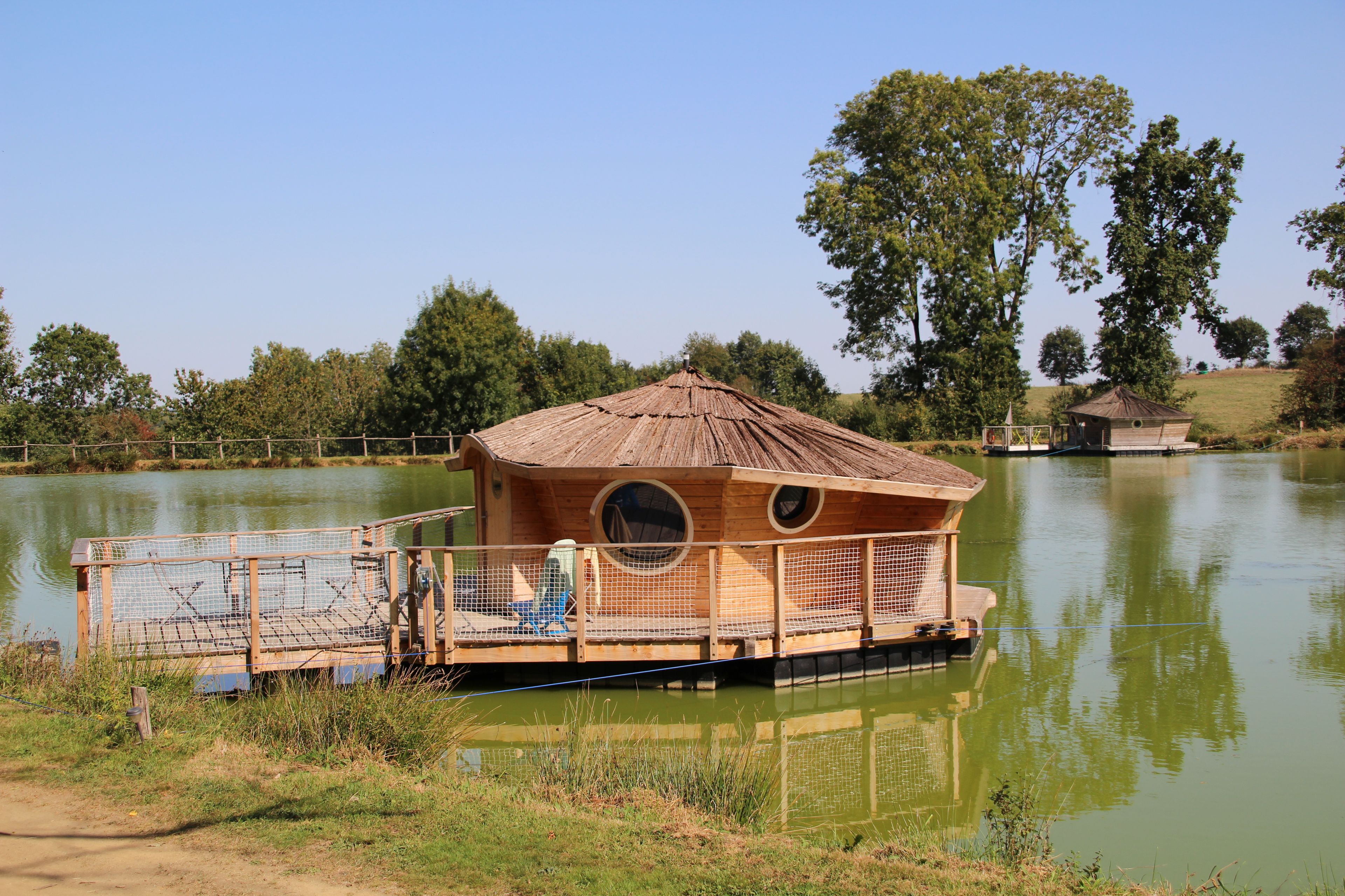 Une construction en bois, dotée d’un toit de chaume, située sur un lac et entourée d’arbres.