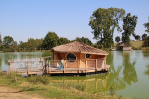 Une construction en bois, dotée d’un toit de chaume, située sur un lac et entourée d’arbres.