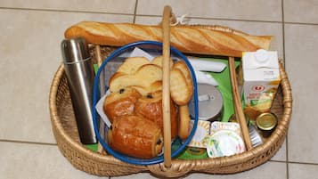Una cesta de mimbre con diversos alimentos, como pan, pasteles y un cartón de jugo de naranja.