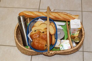 A wicker basket containing various food items, including bread, pastries, and a carton of orange juice. - La Libaudiere (Pouzauges)