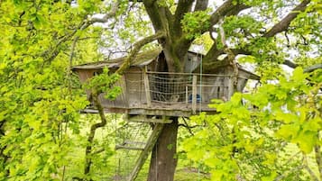 Una casa en el árbol con estructura de madera y una escalera de cuerda.