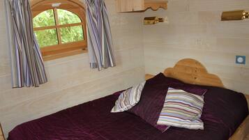 A wooden bed with a purple quilt and striped pillows, a window with curtains, and a wooden headboard.