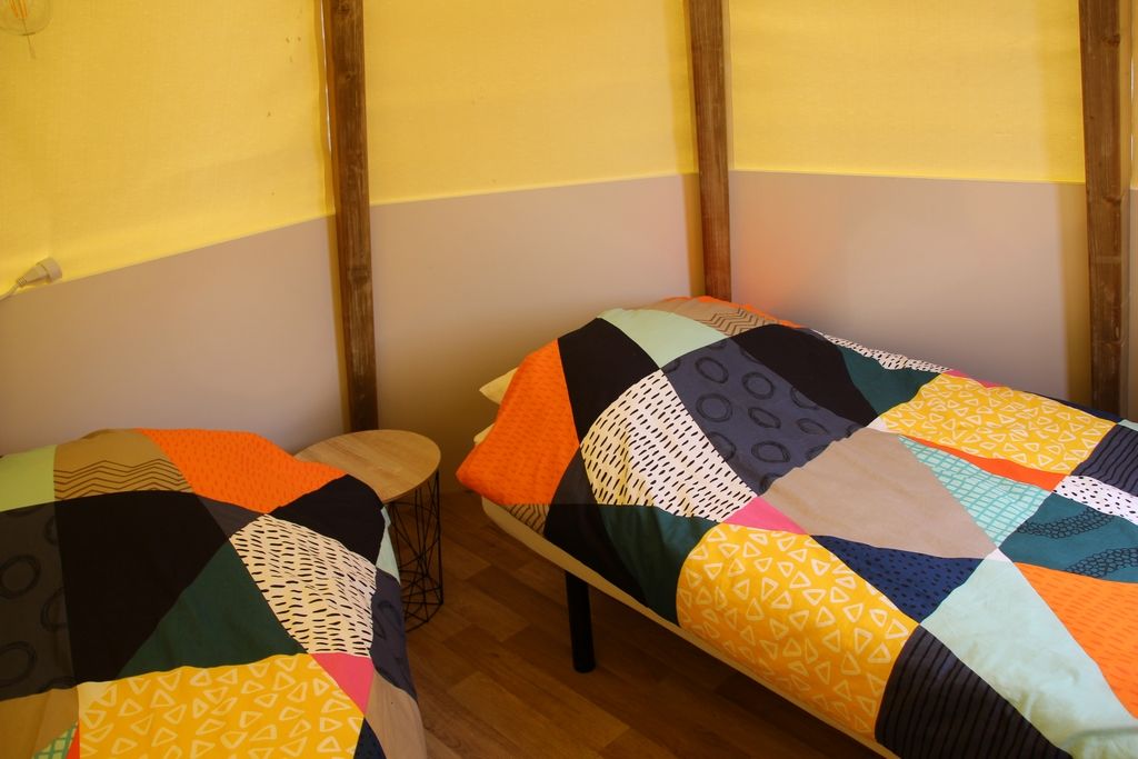 Dos camas individuales con colchas de colores, piso de madera y pared amarilla.