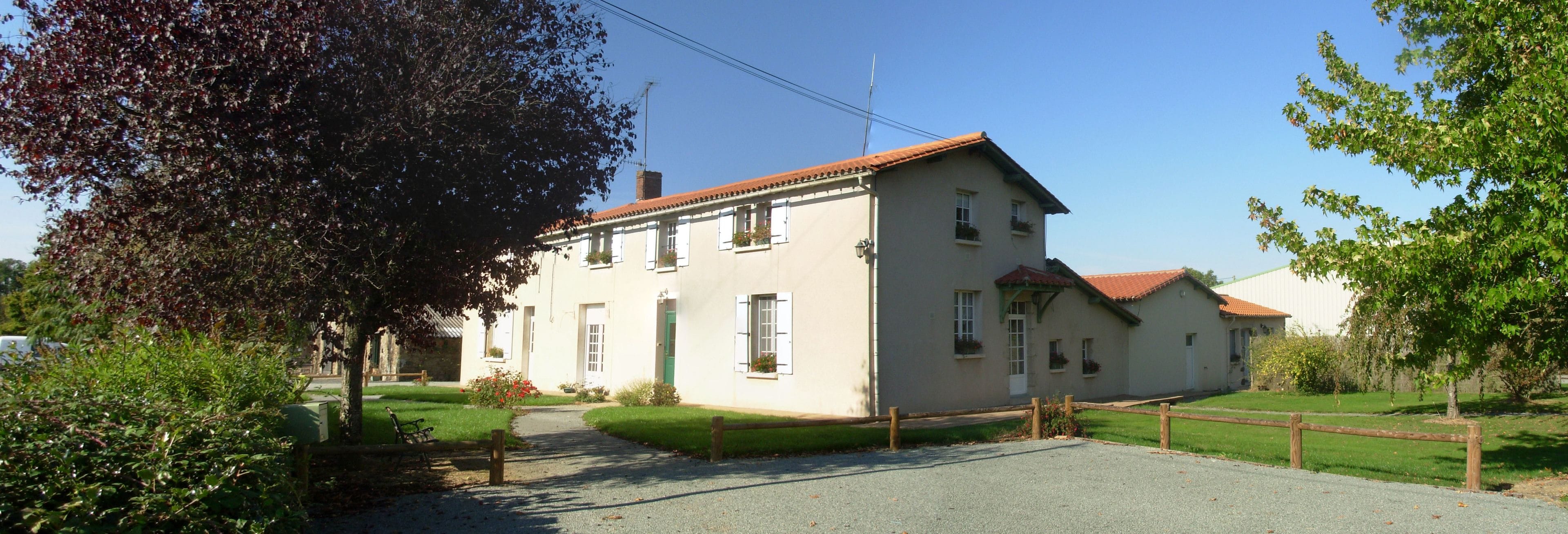 A two-story building with a red-tiled roof, a gravel driveway, and a wooden fence.
