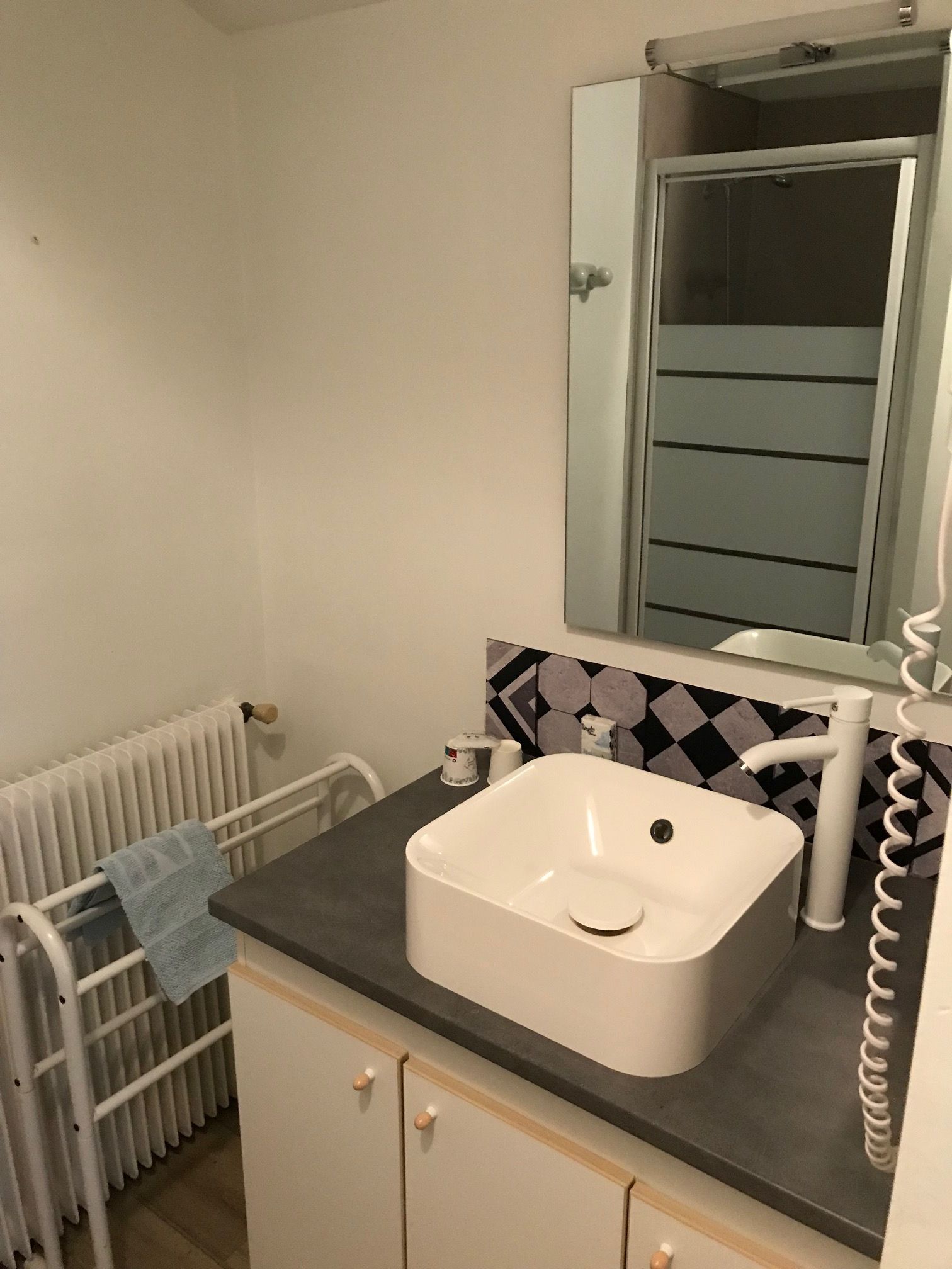 A bathroom with a white sink, a mirror above it, and a towel hanging on a radiator.