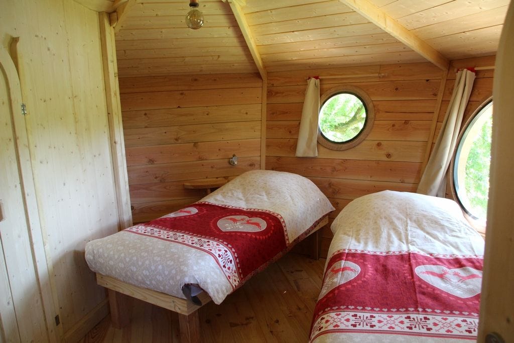 A cabin with two beds, wooden walls, a small window, and a ceiling light.