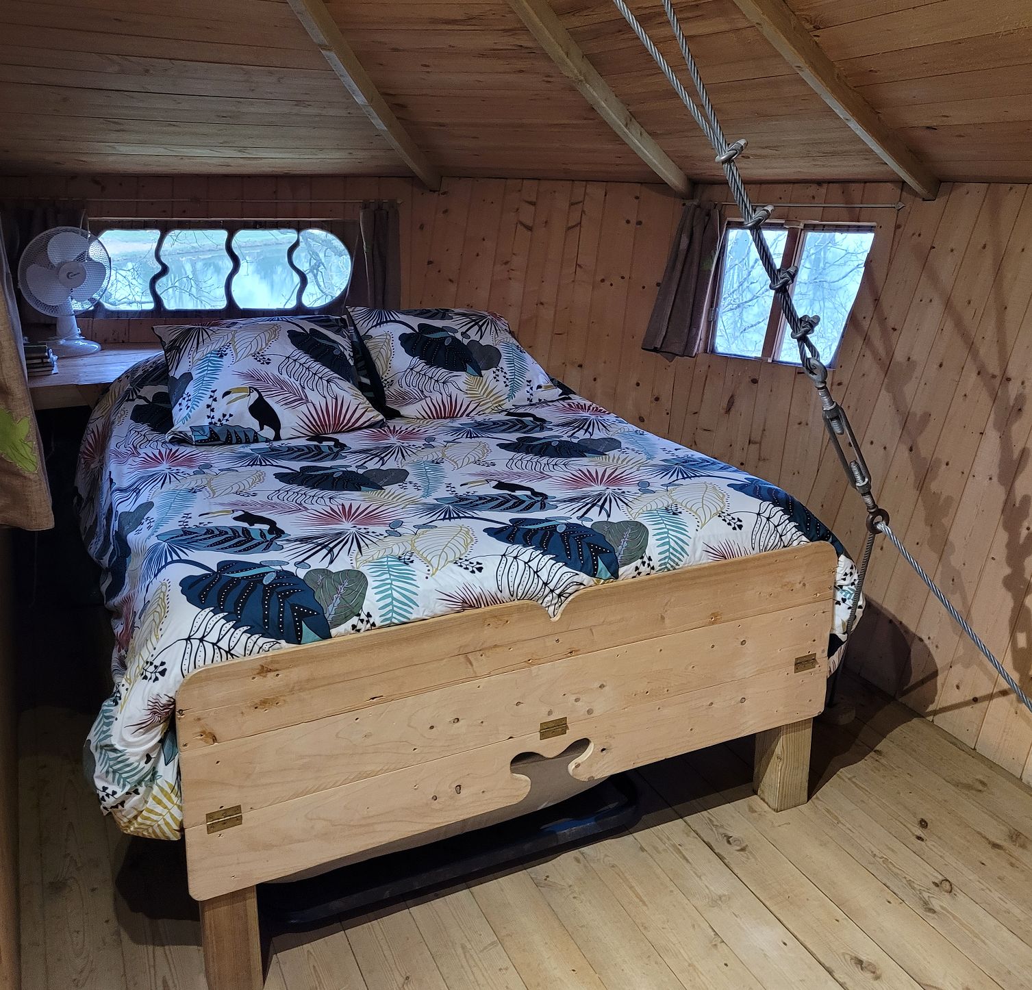 A wooden bed with a floral bedspread in a cabin-style room with wooden walls and a sloped ceiling.