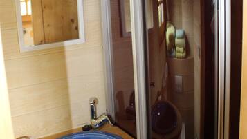 Un baño con tocador de madera, un lavabo azul, un espejo y una cabina de ducha de vidrio.