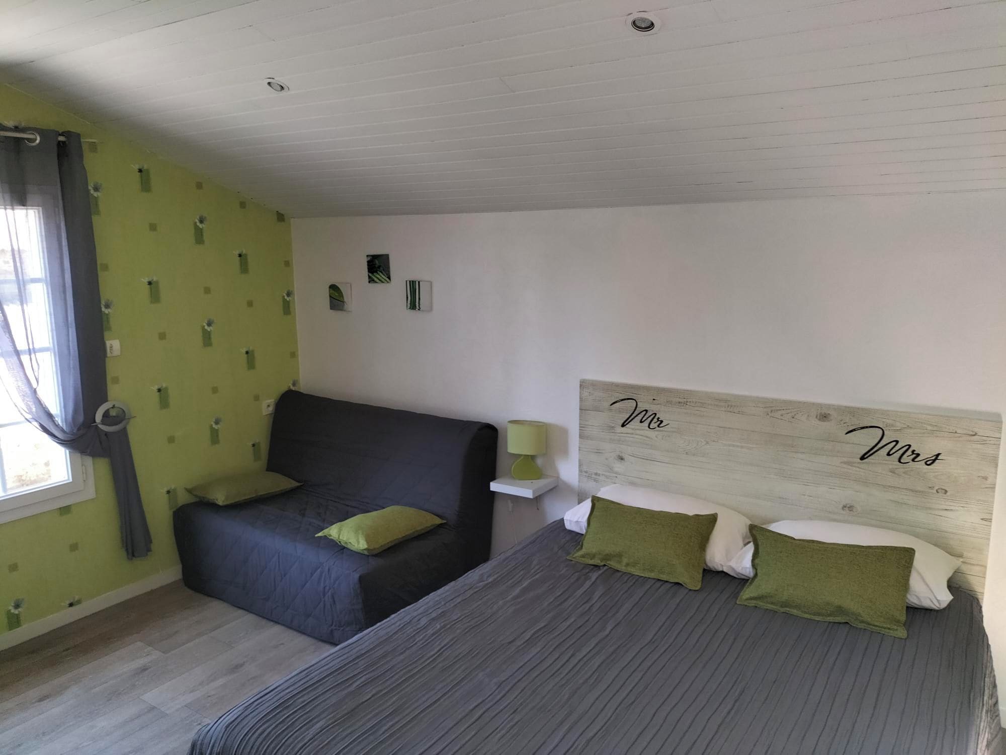 Un dormitorio con cama, sofá, ventana con cortinas y una placa con un nombre en la pared.