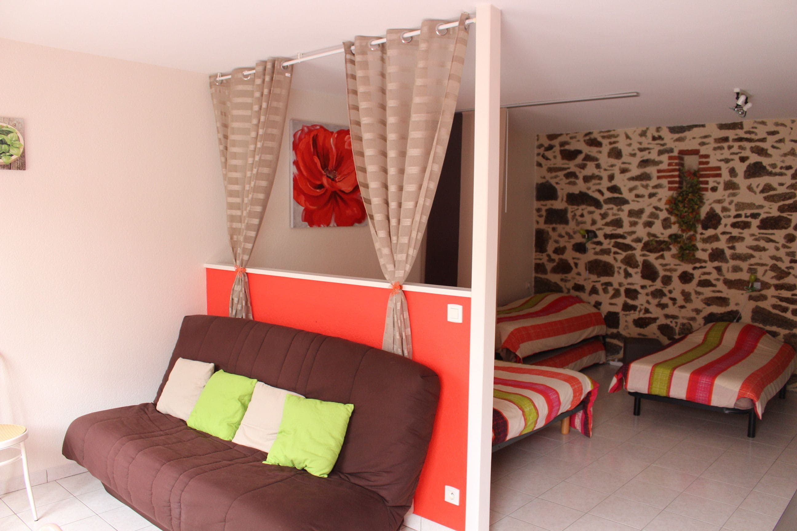 A room with a brown sofa, two single beds with striped bedding, a red flower decoration, and a stone-patterned wall.