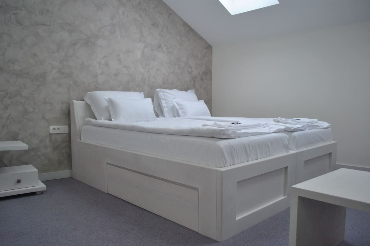 A modern bedroom with a bed, bedside tables, and a skylight.