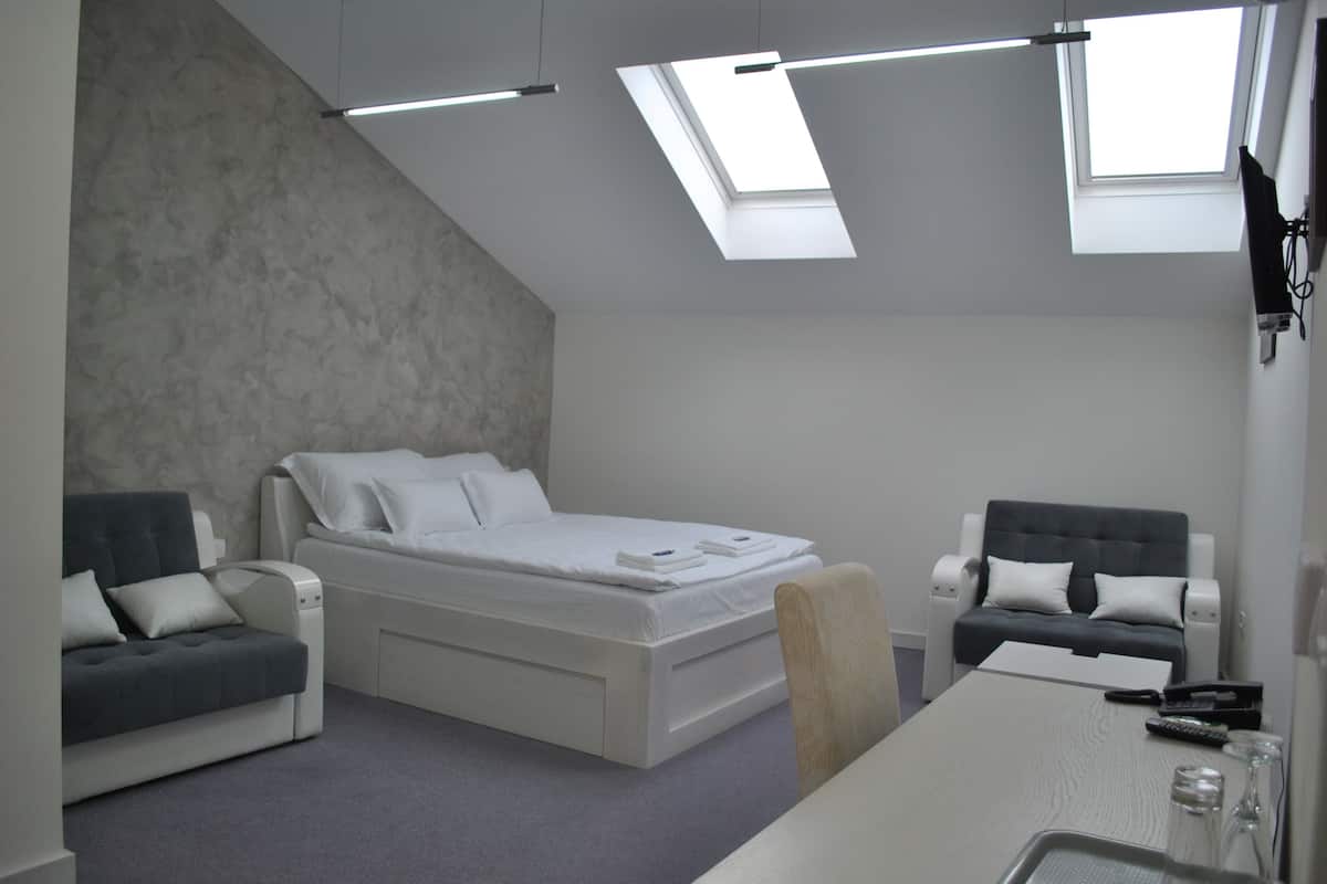 A modern bedroom with a bed, two sofas, a dining table, and skylights.