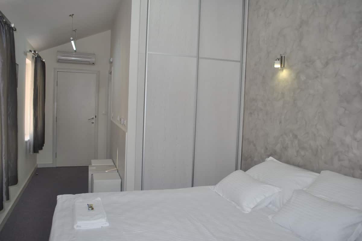 A hotel room with a bed, a wardrobe, a mirror, and a wall-mounted light fixture.