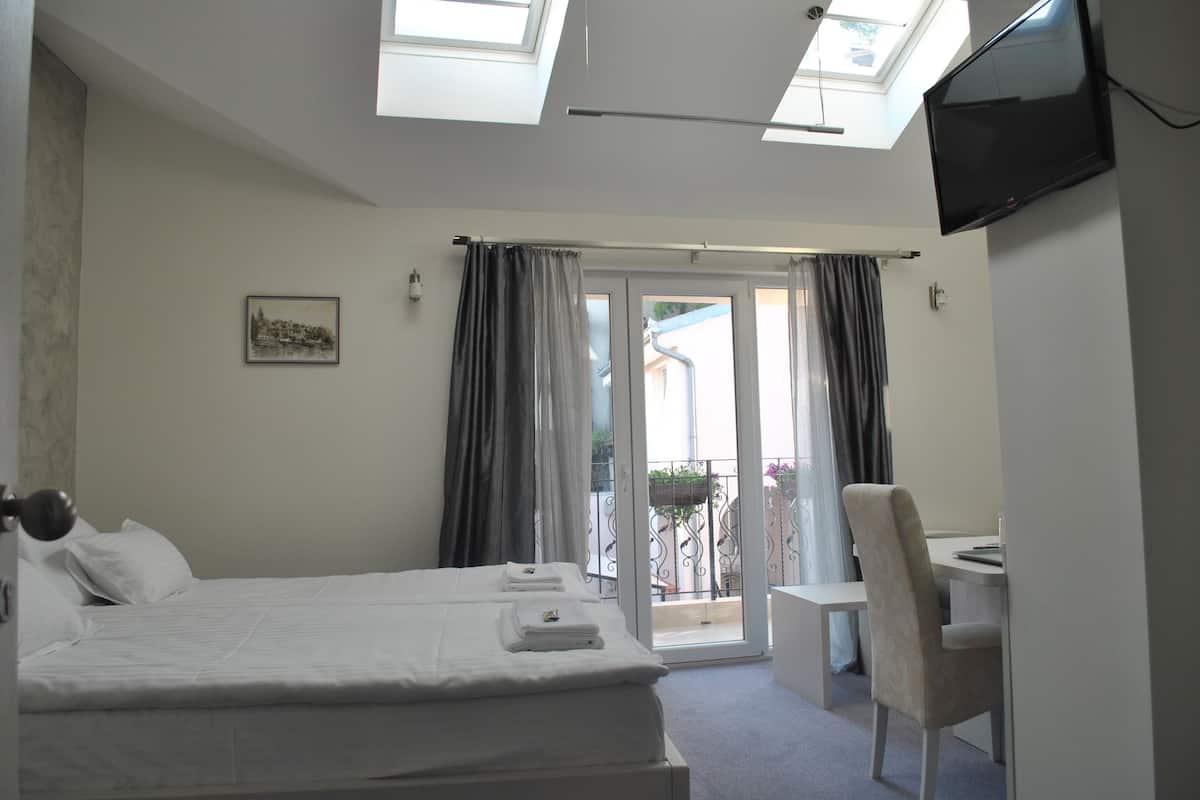 A hotel room with a bed, a desk, a chair, a TV, and a balcony with curtains.