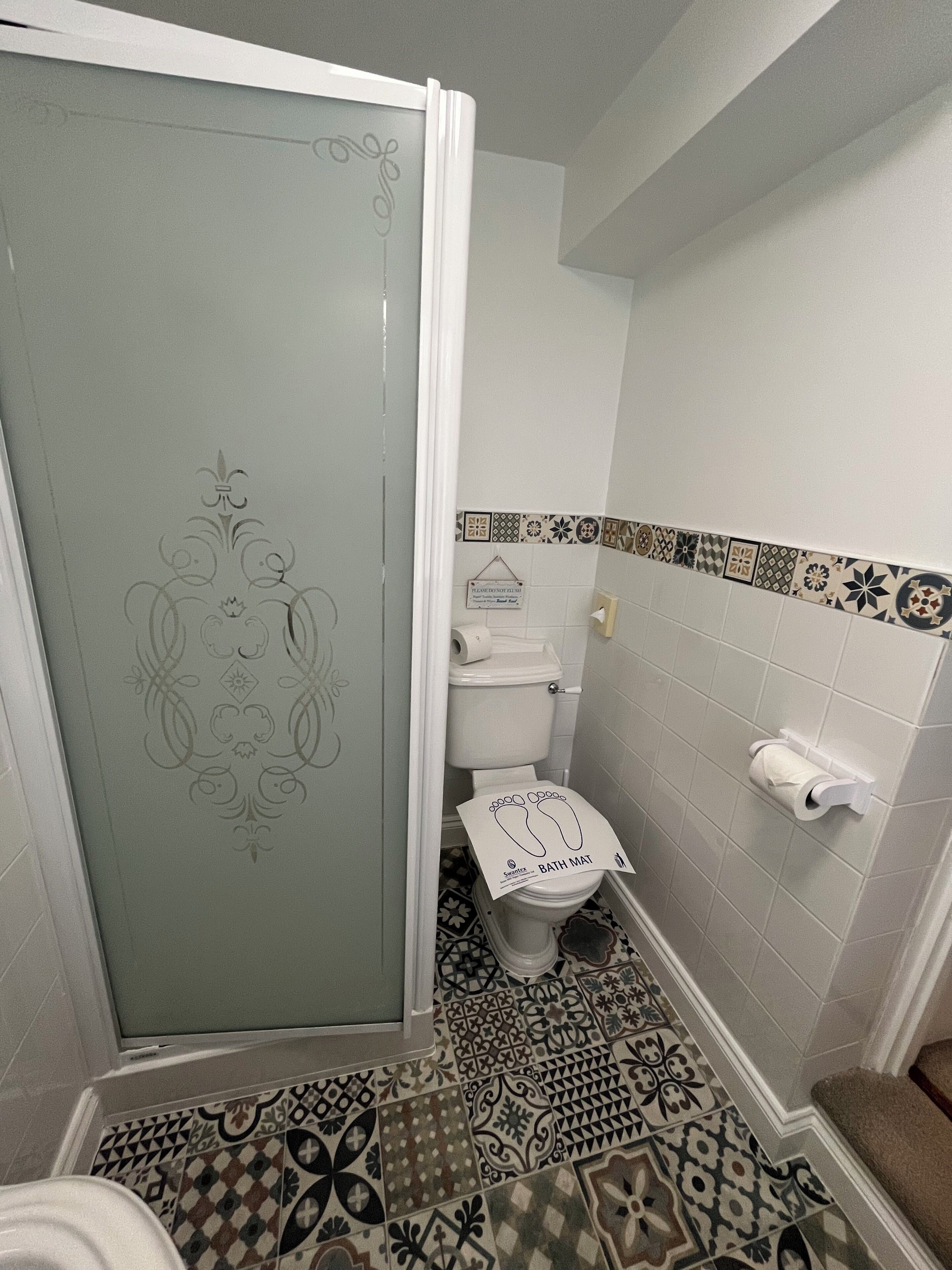 Een badkamer met toilet, douche en vloertegels met een patroon.