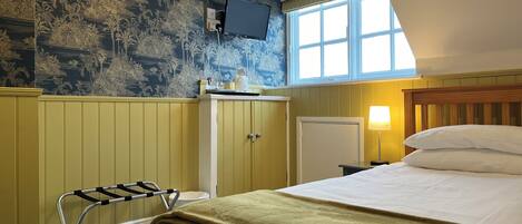 A hotel room with a bed, a TV mounted on the wall, a window with a view, and a wooden cabinet.