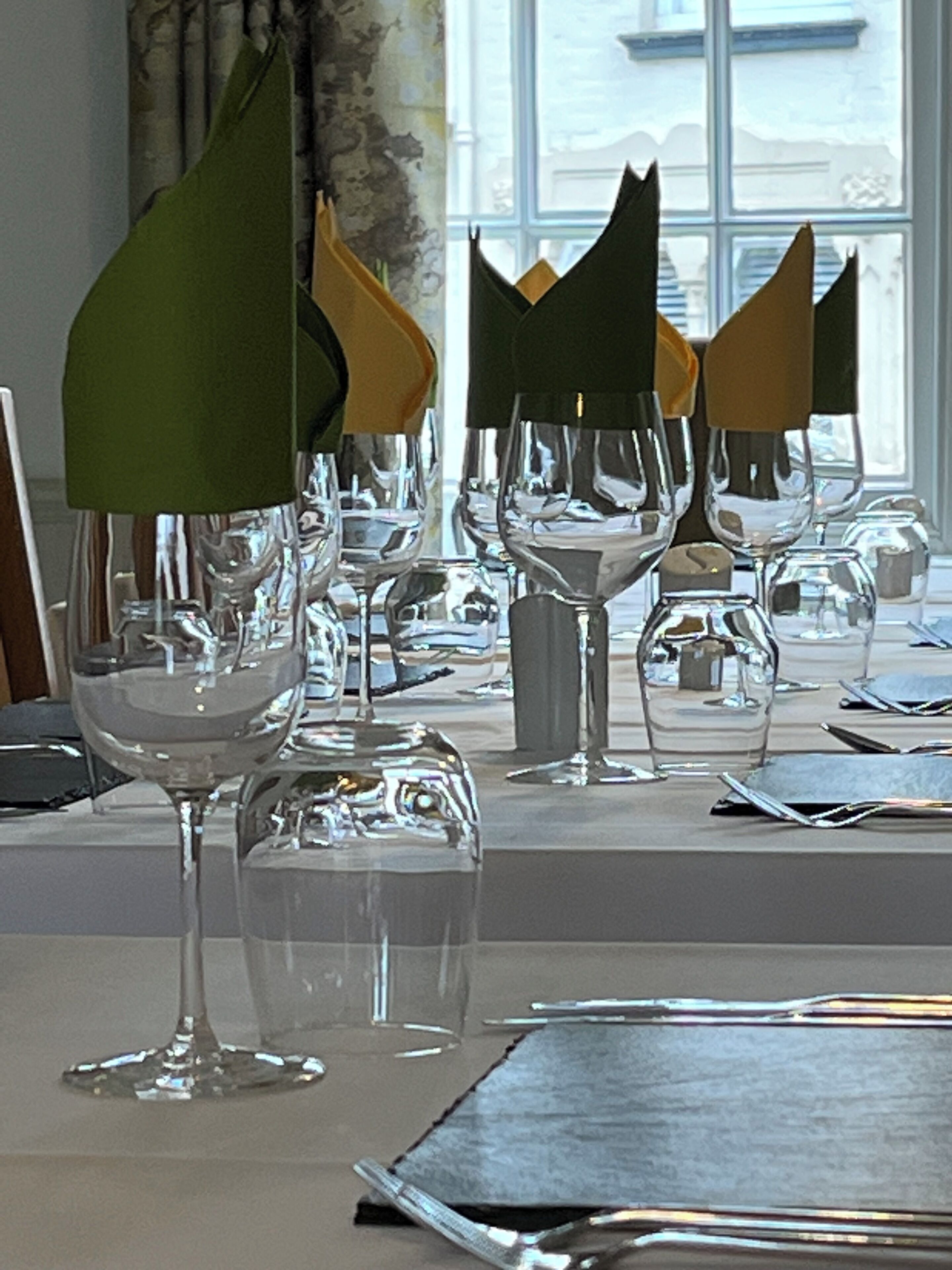 A dining area with multiple tables set with wine glasses and napkins.