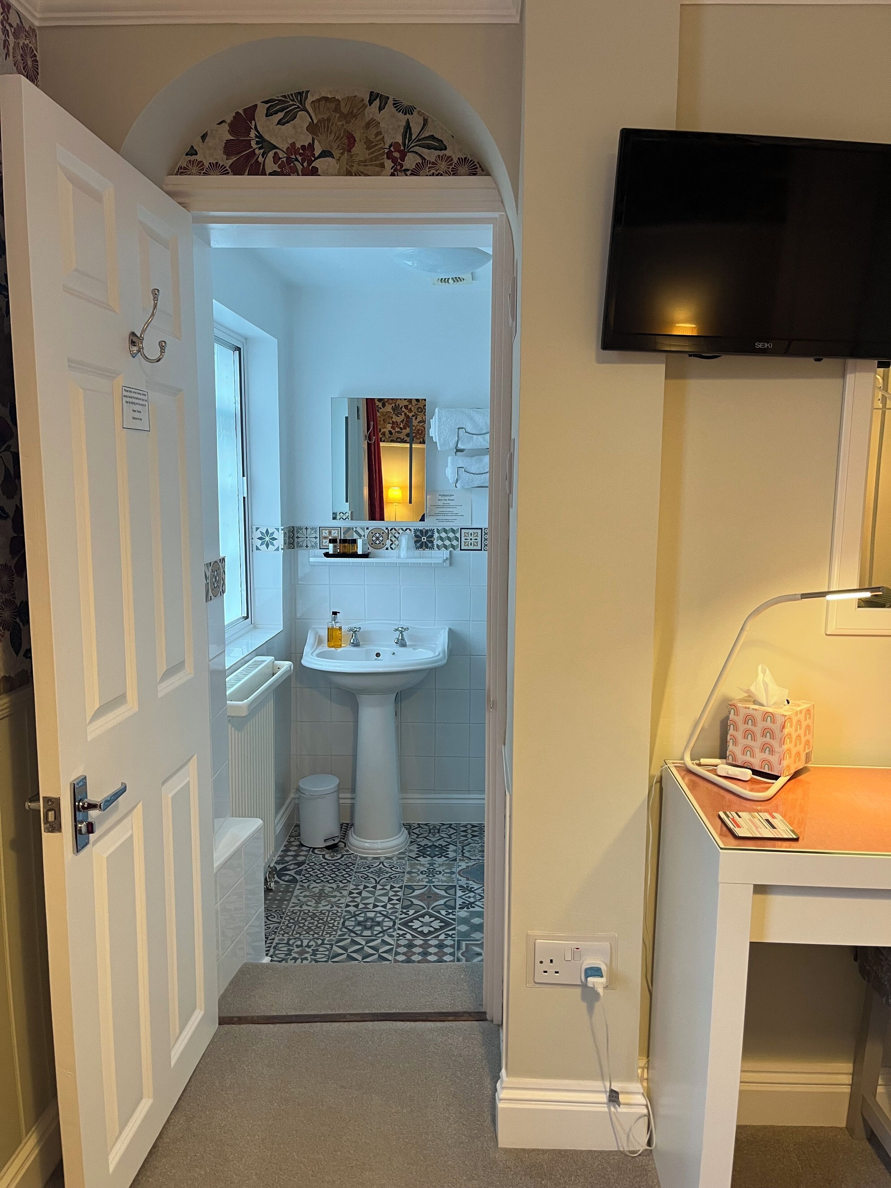 A bathroom with a white sink, a mirror, a towel rack, and a television mounted on the wall.