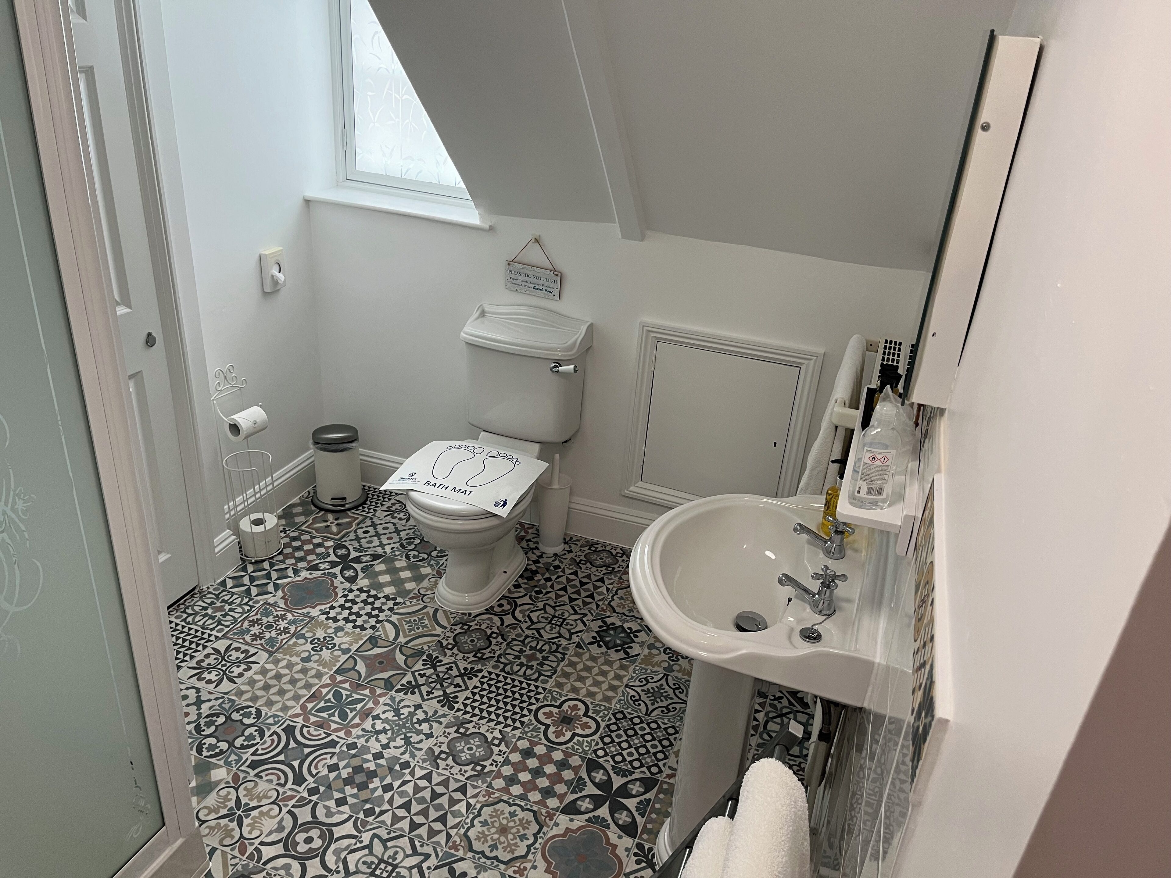 A bathroom with a toilet, sink, and patterned floor tiles.
