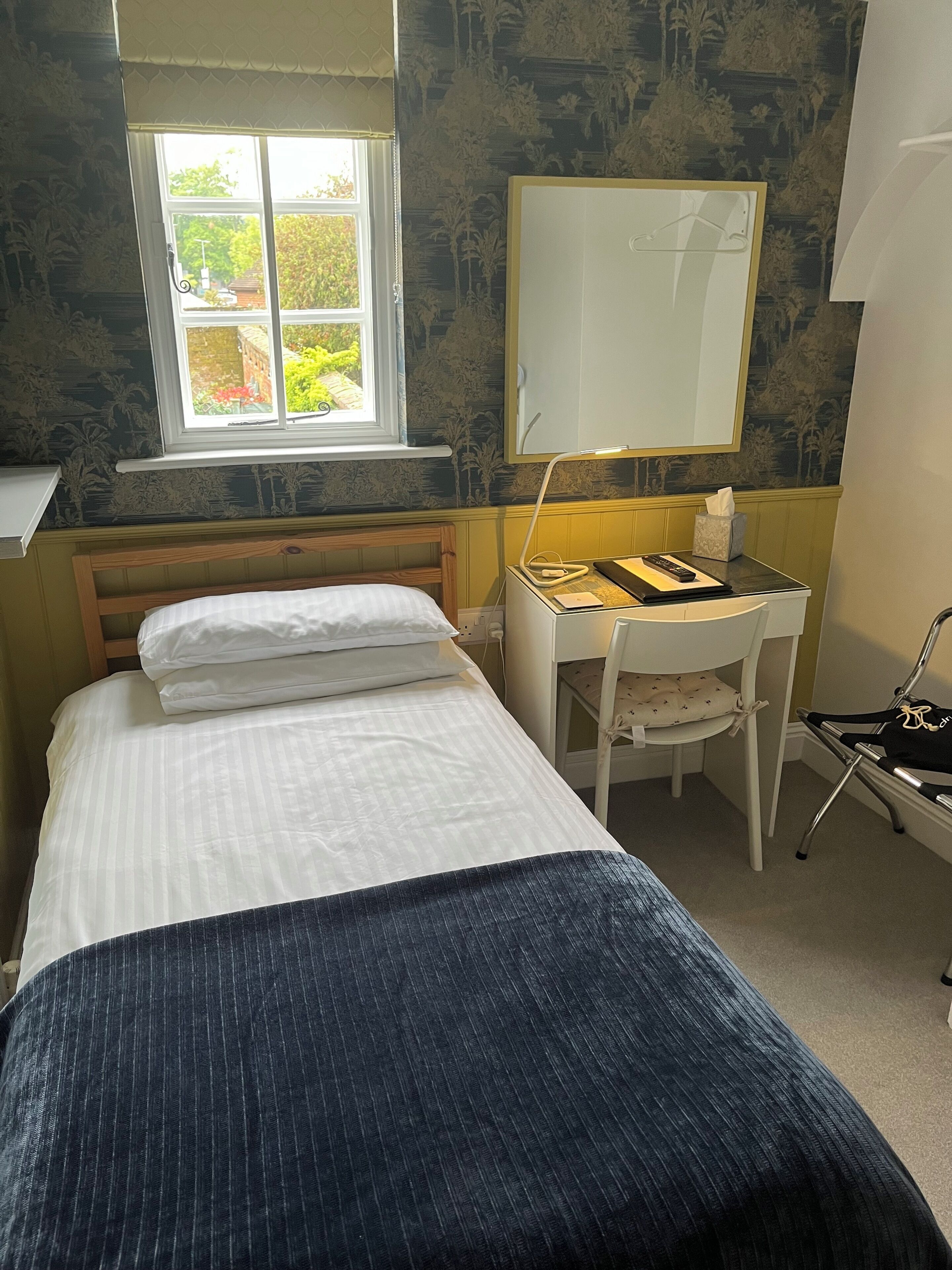 A bedroom with a bed, a desk, a chair, a window, and a mirror.