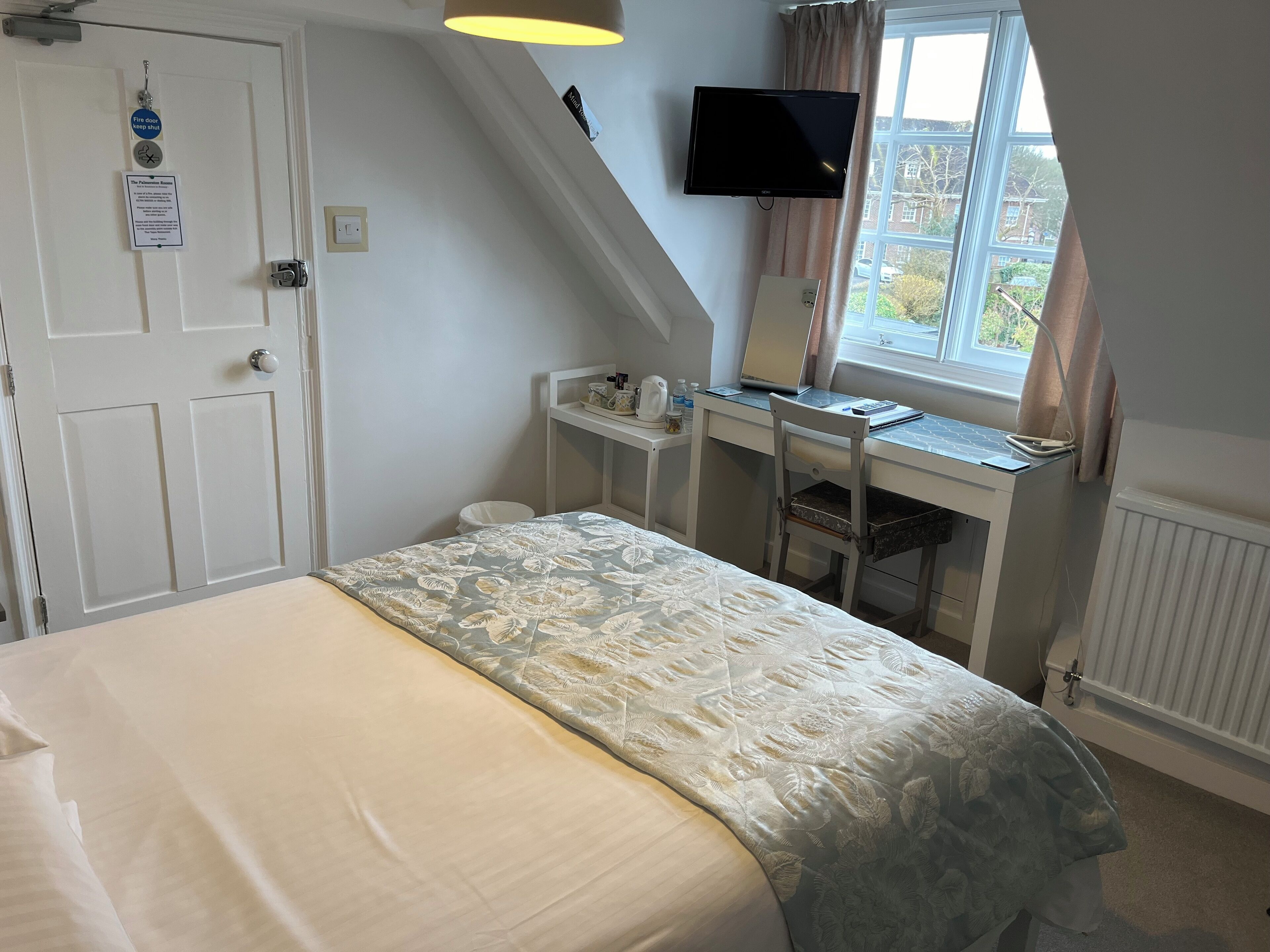 A bedroom with a bed, a desk, a chair, a television, and a window with curtains.