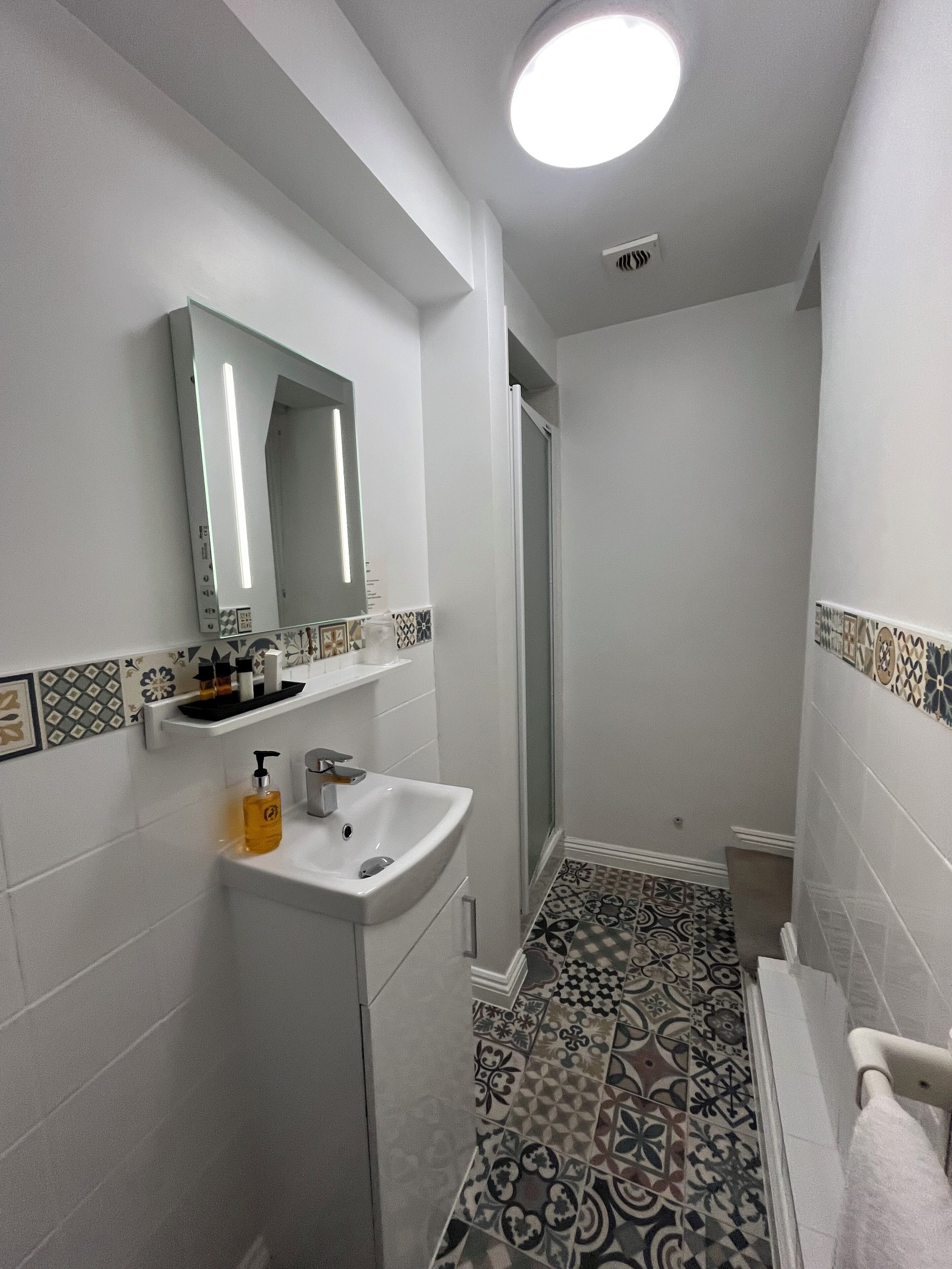 A bathroom with a white sink, mirror, and patterned floor tiles.