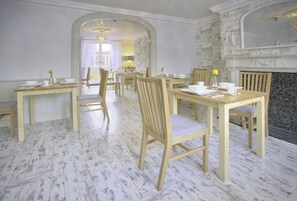 A dining area with wooden tables and chairs, a fireplace, and a stone wall. - The Palmerston Rooms (Romsey)