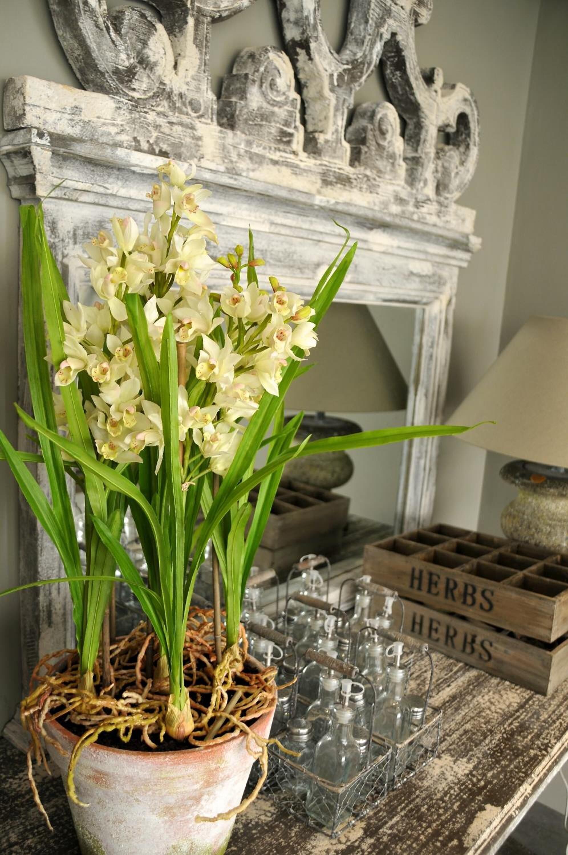 A rustic setting with a potted orchid plant, a wooden crate labeled "HERBS," and a vintage metal rack with glassware.