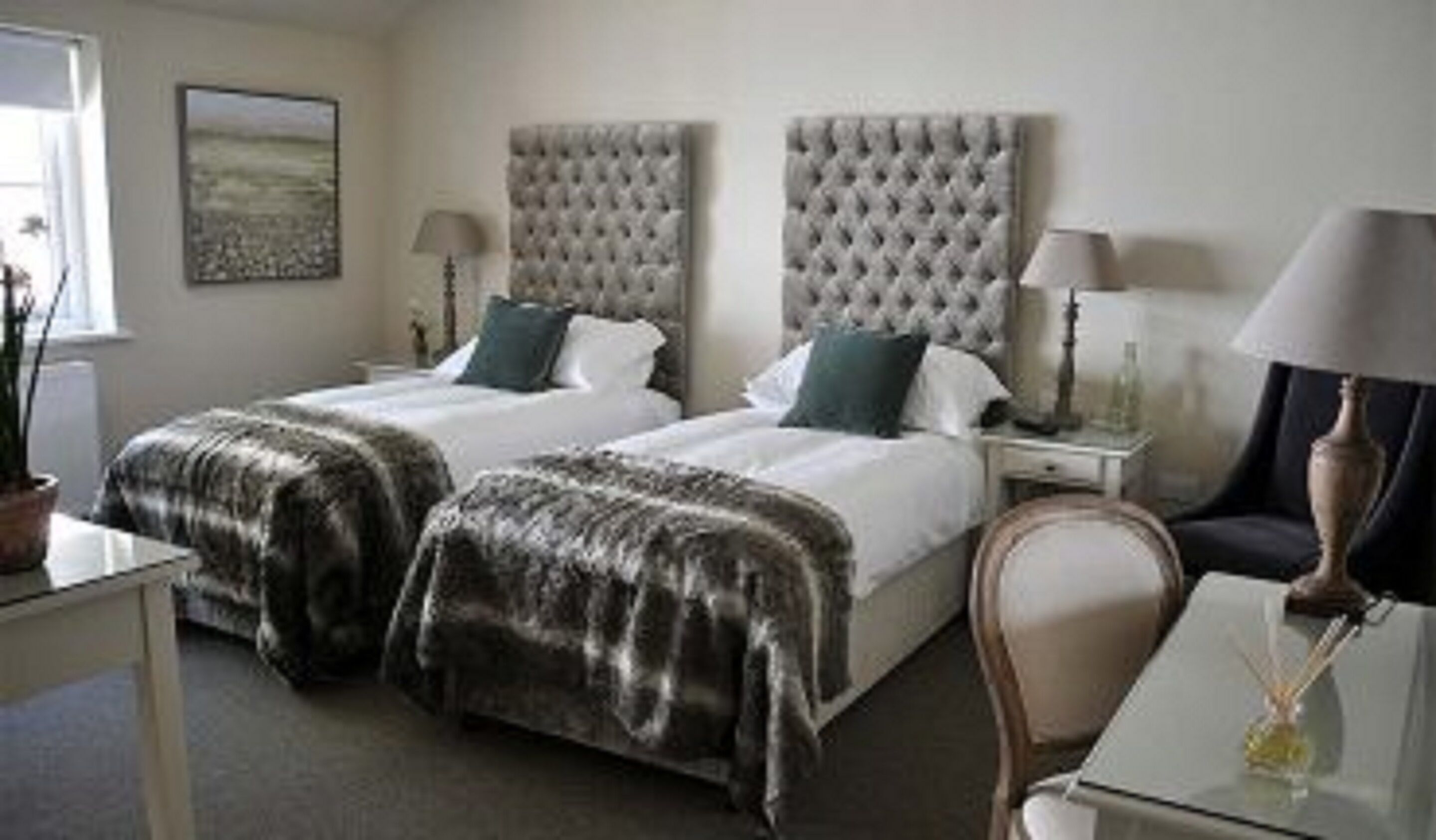 A hotel room with two beds, a desk, a chair, and a lamp.