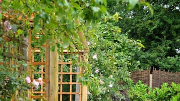 Une terrasse de jardin agrémentée d’une treille en bois, d’un sol en pierre et de meubles en osier.