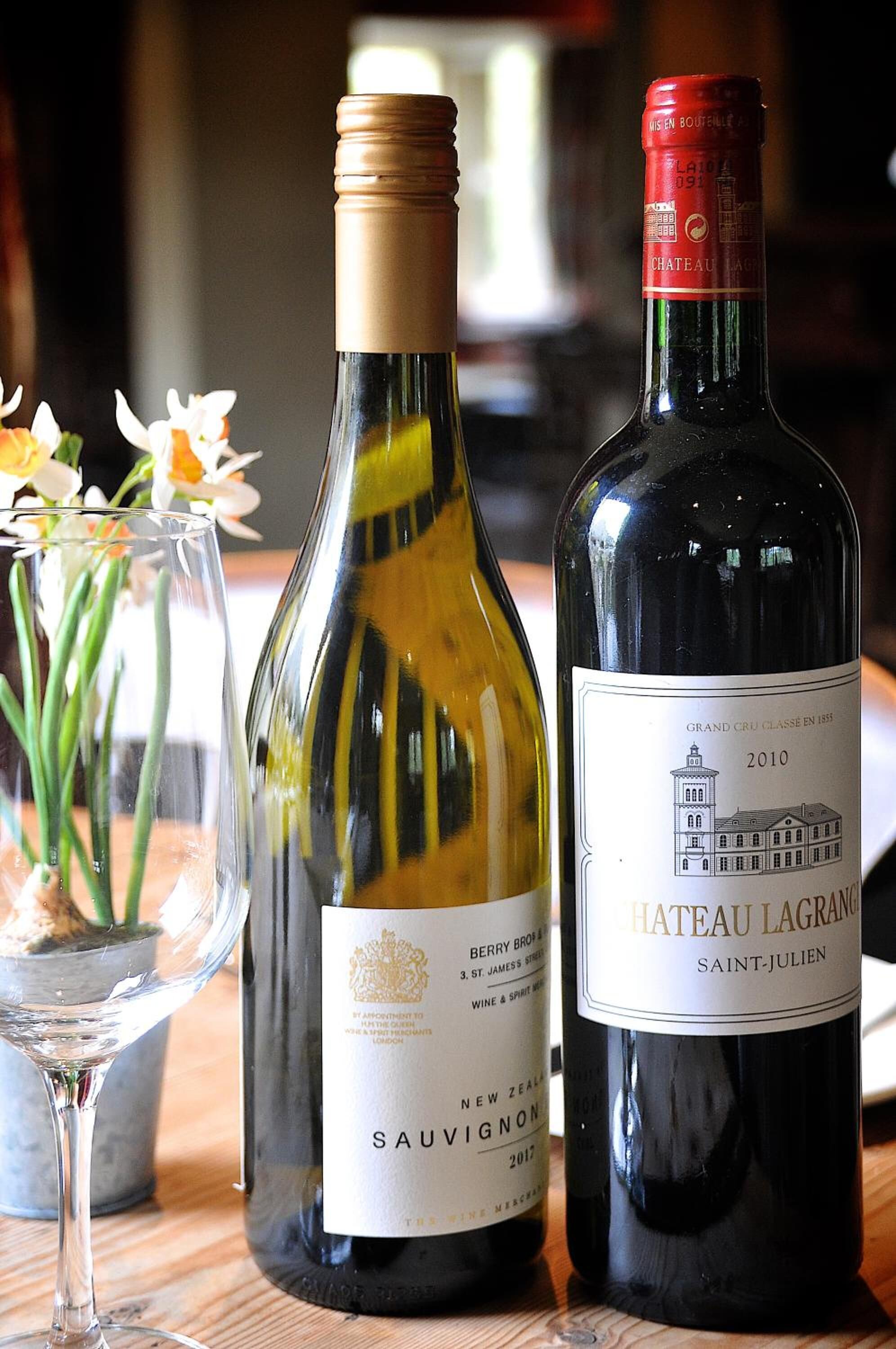 Tres botellas de vino sobre una superficie de madera, con una copa y flores al frente.