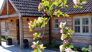 A wooden log cabin with a tiled roof, a front porch, and a small garden area with potted plants. - The Red Lion Inn (Somerton)