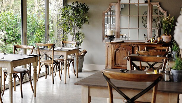 A dining area with wooden tables and chairs, large windows, and a mirror with Roman numerals. - The Red Lion Inn (Somerton)