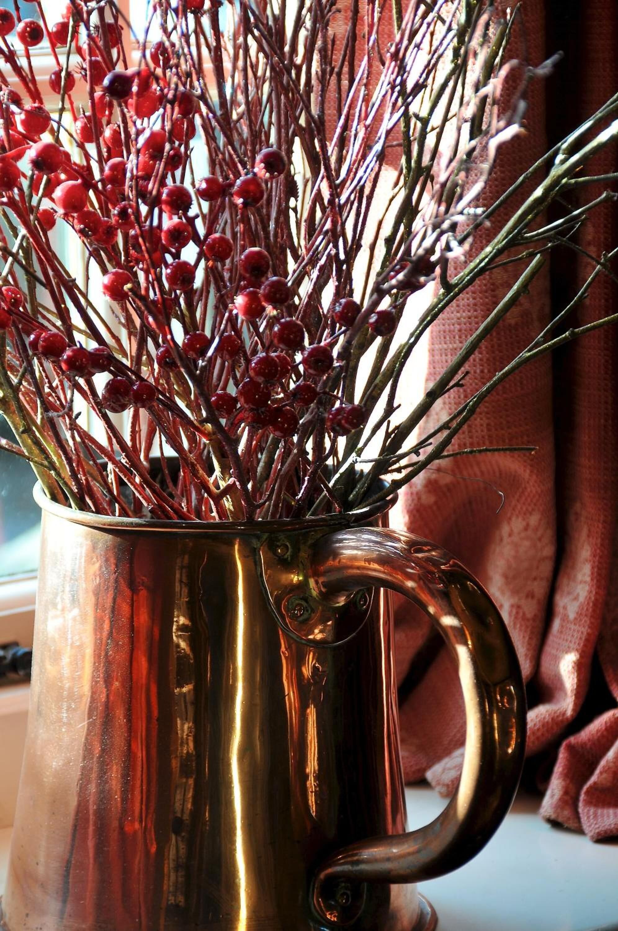 A copper mug filled with red berries and branches.