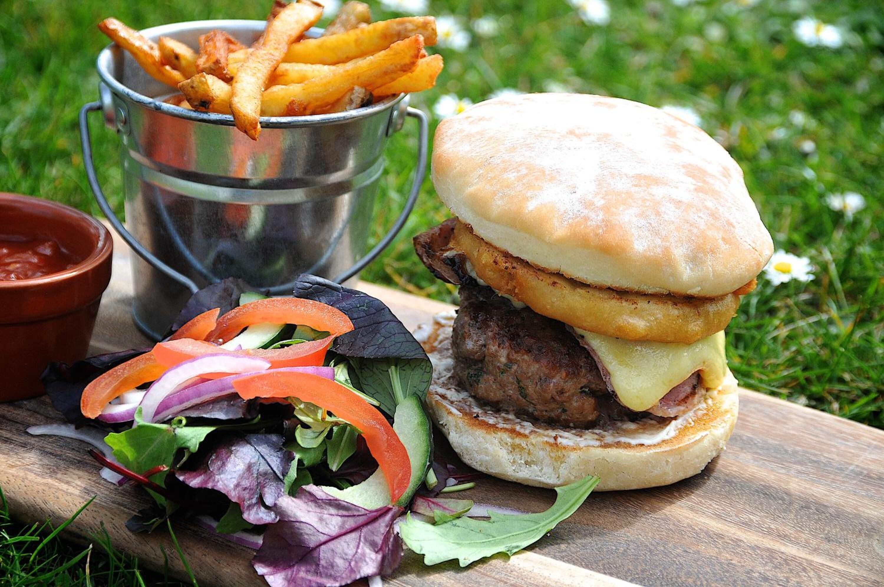A burger with a side of fries and salad on a wooden board.