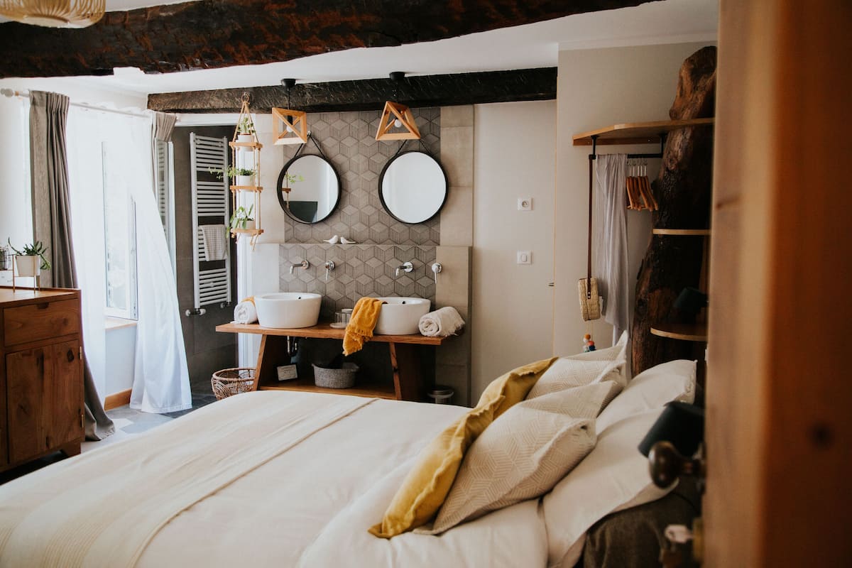 A bedroom with a large bed, a wooden dresser, a vanity with a mirror, and a rustic ceiling.