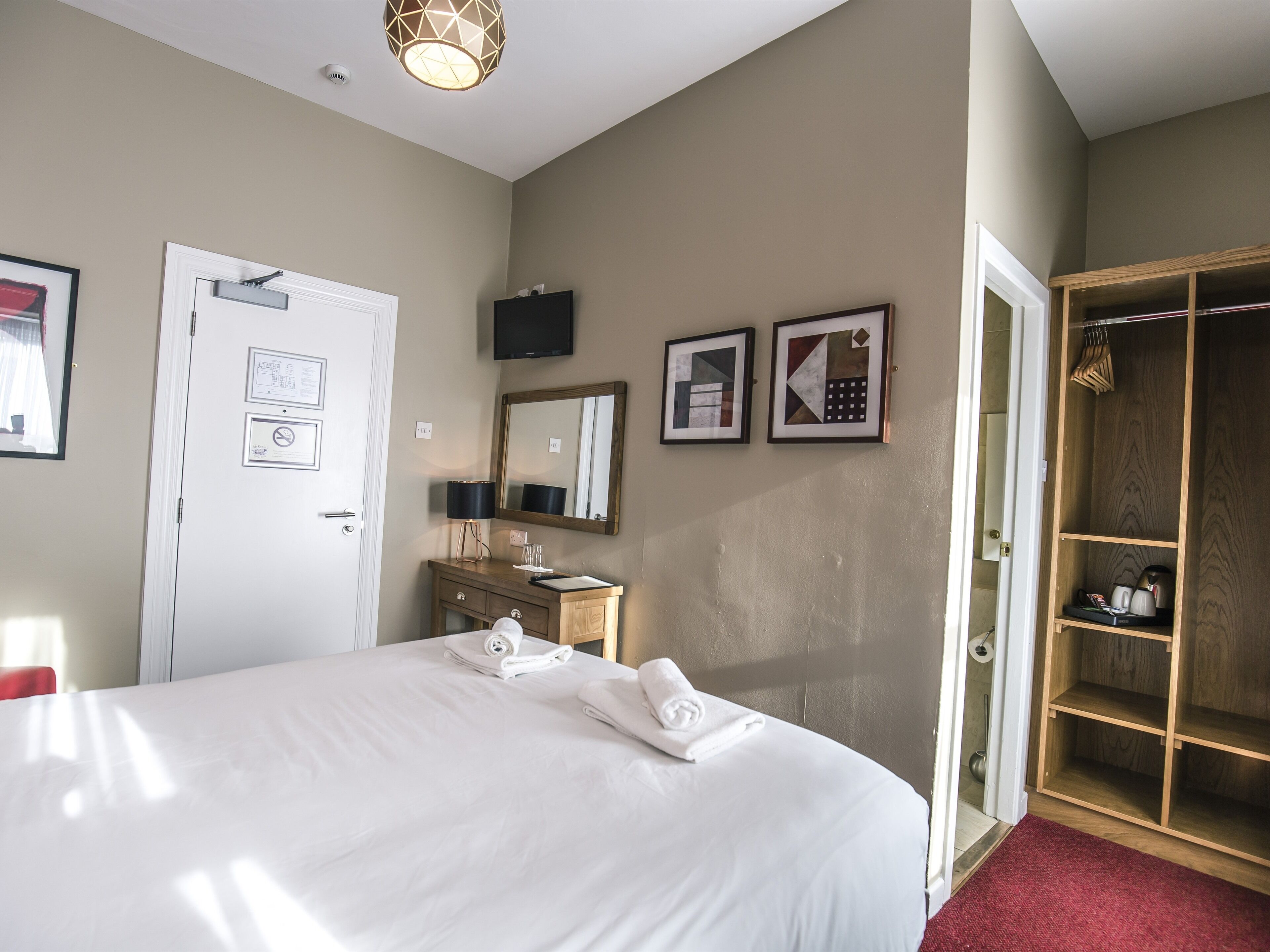 Una camera d'albergo con un letto grande, un armadio in legno, una toeletta con specchio e opere d'arte incorniciate al muro.
