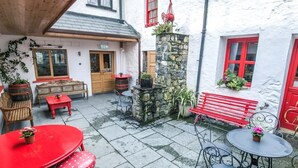 Un patio con suelo de piedra, mobiliario de metal rojo y negro, y una pared de piedra con una chimenea.