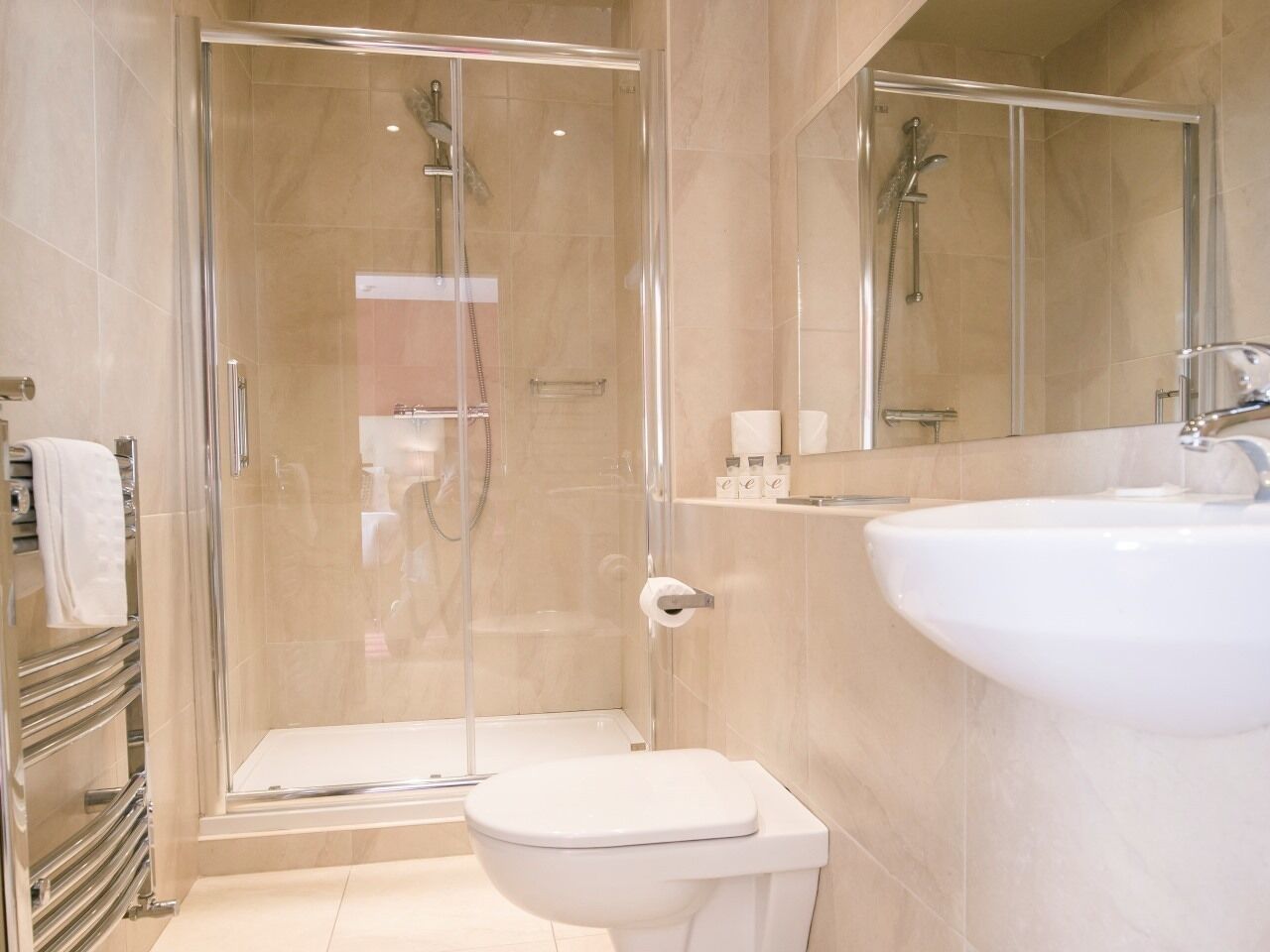 A modern bathroom with a glass-enclosed shower, a white toilet, and a sink with a mirror above it.
