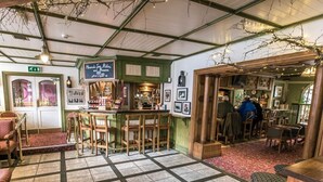 Un pub acogedor con barra, mobiliario de madera y suelo de baldosas.